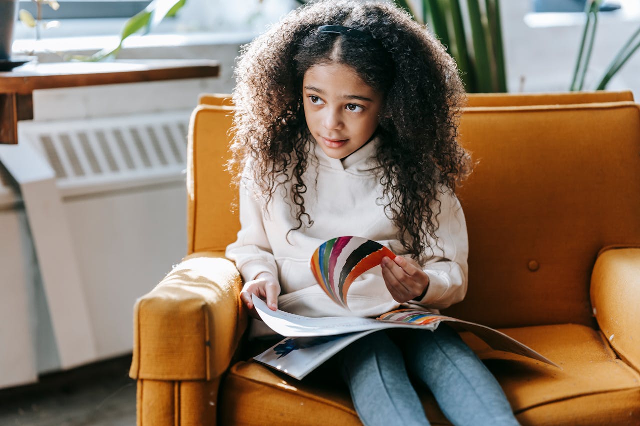 Sweet black girl reading book on cozy armchair